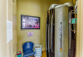 Stand up tanning bed in right of room, chair to left with a beach photo above.